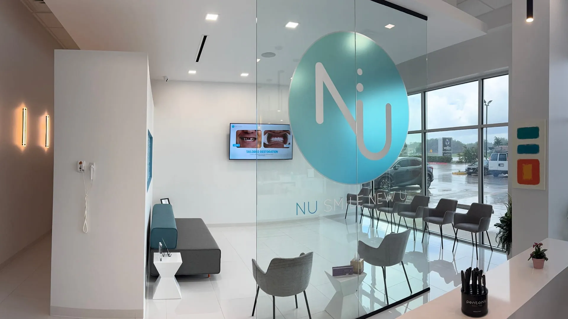 Nu Dentistry waiting room viewed through branded glass partition with logo and seating